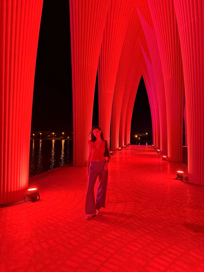 Maram standing in a corridor of glowing red arches at night