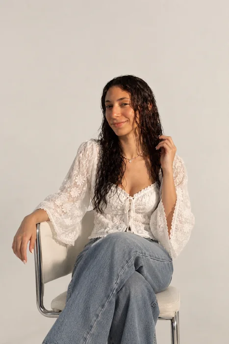 Maram sitting on a chair in a white lace blouse